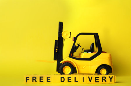 Toy forklift and cubes with words FREE DELIVERY on yellow background. Logistics and wholesale conceptの写真素材
