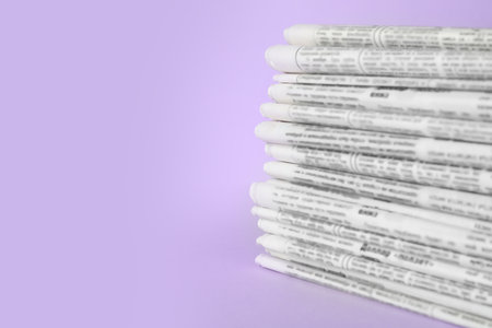 Stack of newspapers on light violet background, space for text. Journalist's workの写真素材