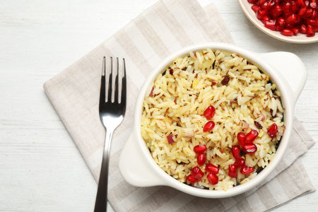 Tasty rice pilaf with pomegranate grains served on white wooden table, flat layの写真素材