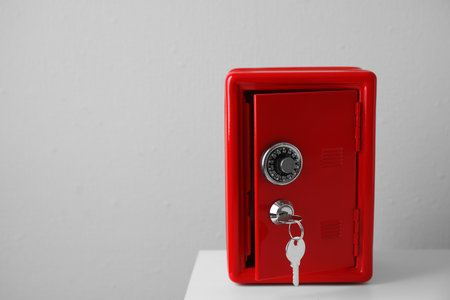 Red steel safe with keys on table against light wall. Space for textの写真素材