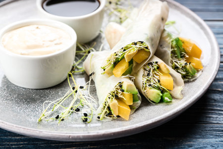 Delicious rolls wrapped in rice paper served on blue wooden table, closeup