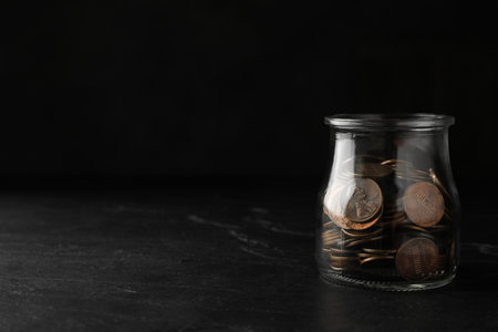 Glass jar with coins on black table, space for textの写真素材