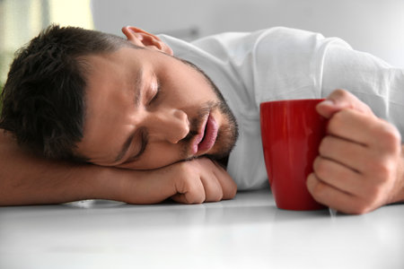 Man with cup of drink sleeping at home in the morningの写真素材