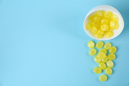 Delicious lemon drops and bowl on light blue background, flat lay. Space for textの写真素材