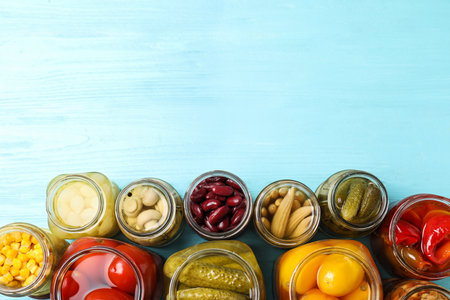 Glass jars with different pickled vegetables on light blue wooden table, flat lay. Space for textの写真素材