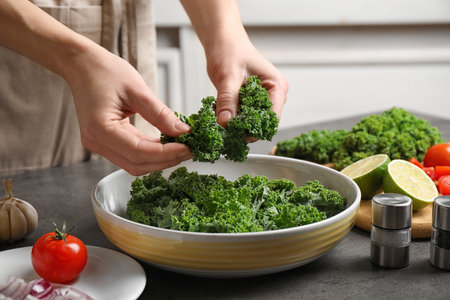 Woman cooking tasty kale salad on gray table, closeupの写真素材