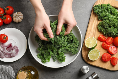 Woman cooking tasty kale salad on gray table, top viewの写真素材