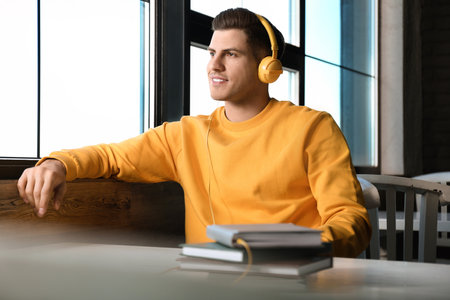 Man with headphones connected to book at table in cafe