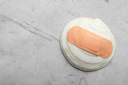Shell with sticking plaster on light gray stone table, top view. Space for text
