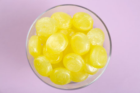 Tasty lemon drops in bowl on violet background, top viewの写真素材