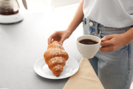 Woman having tasty breakfast with croissant and coffee at home, closeup. morning routineの写真素材