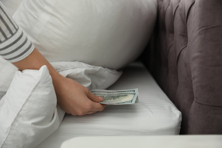 Woman hiding dollar banknotes under pillow in bedroom, closeup. money savingsの写真素材