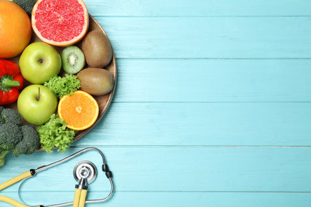 Fruits, vegetables and stethoscope on light blue wooden background, flat lay with space for text....