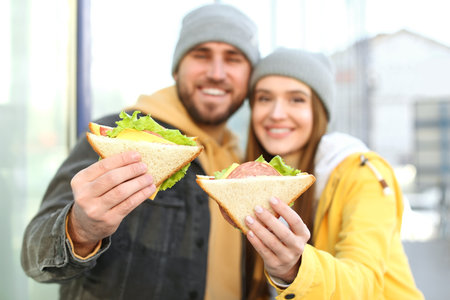 Happy young couple with sandwiches on city streetの写真素材