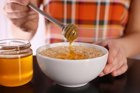 Woman adding honey to oatmeal at black table, closeupの写真素材