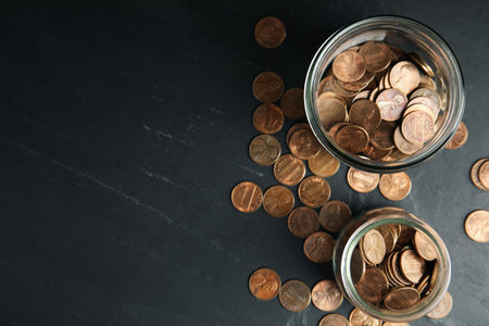 Glass jars with coins on black table, flat lay. Space for textの写真素材
