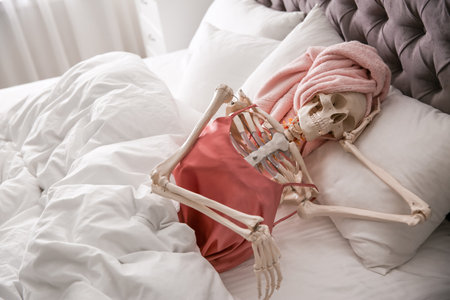 Human skeleton in silk pajamas and towel lying on bed indoorsの写真素材