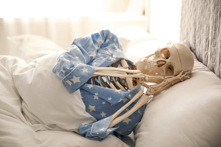 Human skeleton in pajamas lying on bed indoorsの写真素材