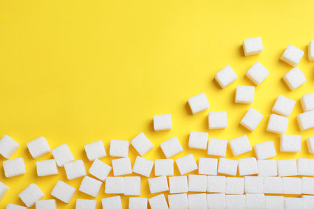 Refined sugar cubes on yellow background, top view. Space for text
