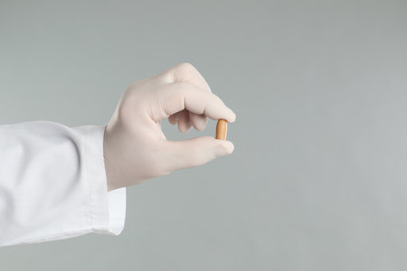 Doctor holding suppository for hemorrhoid treatment on light gray background, closeupの写真素材
