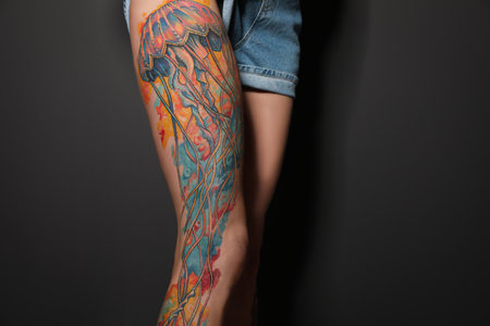 Woman with tattoos on leg against black background, closeupの写真素材