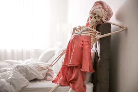 Human skeleton in silk pajamas and towel sitting on bed indoorsの写真素材