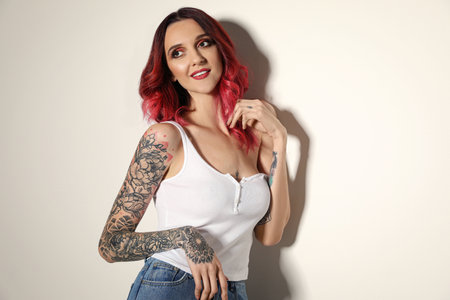 Beautiful woman with tattoos on arms against light backgroundの写真素材