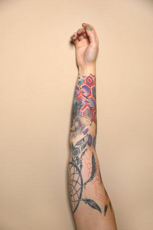 Woman with colorful tattoos on arm against beige background, closeupの写真素材