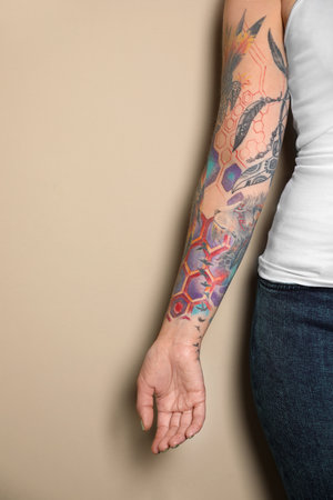 Woman with colorful tattoos on arm against beige background, closeupの写真素材