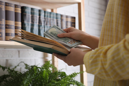 Woman hiding dollar banknotes in book indoors, closeup. money savingsの写真素材