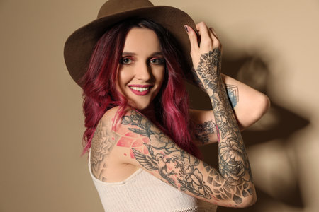 Beautiful woman with tattoos on arms against beige backgroundの写真素材