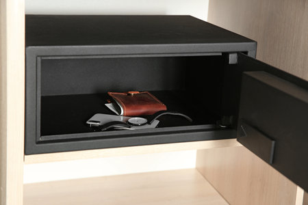 Open steel safe with wallet, watch and smartphone in wooden closet at hotelの写真素材