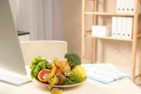 Nutritionist's workplace with fruits, vegetables and measuring tape on tableの写真素材