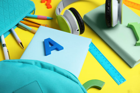 Books, headphones and school stationery on yellow background