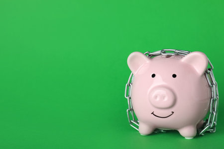 Piggy bank with steel chain on green background, space for text. money safety conceptの写真素材