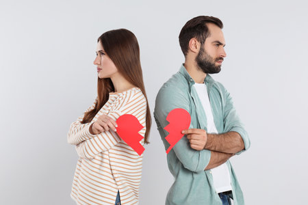 Couple with torn paper heart on light background. relationship problems