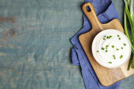 Fresh sour cream with onion on light blue wooden table, flat lay. Space for textの写真素材