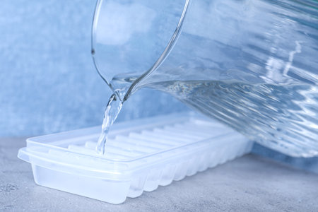 Pouring water into ice cube tray on light gray table, closeupの写真素材