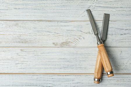 Modern chisels on white wooden background, flat lay with space for text. Carpenter's tools