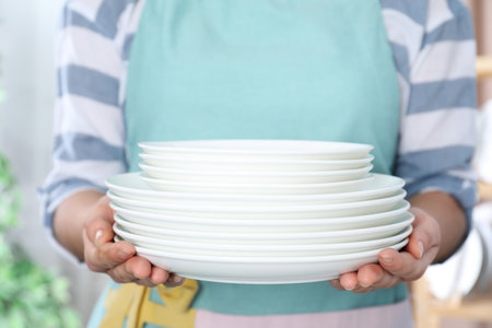 Woman holding stack of clean plates on blurred background, closeupの写真素材