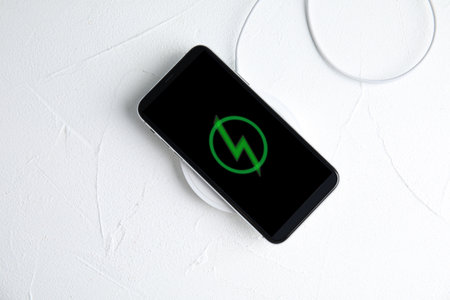 Mobile phone charging with wireless pad on white stone table, top viewの写真素材