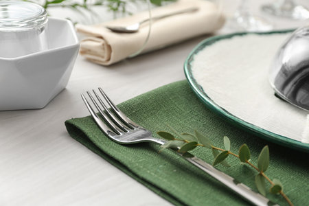 Stylish clean fork with leaves on white table, closeup. Festive setting