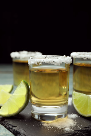 Mexican Tequila shots, lime slices and salt on blue wooden table