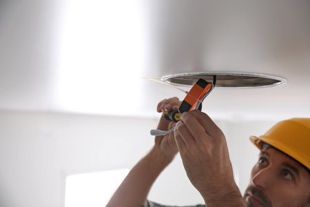 Worker repairing lamp on stretch ceiling indoors. Space for textの写真素材