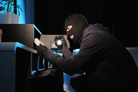 Thief taking money out of steel safe indoors at night