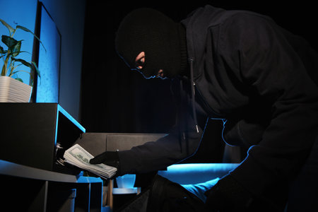 Thief taking money out of steel safe indoors at night