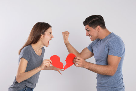 Couple with torn paper heart quarrelling on light background. relationship problems