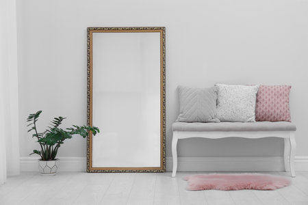 Modern large mirror and comfortable bench near light wall in room
