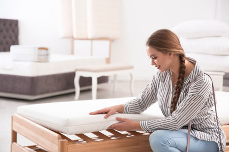 Young woman touching mattress in furniture store. Space for textの写真素材