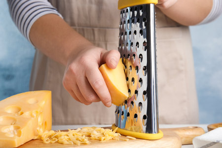 Woman grating fresh cheese at table, closeupの写真素材